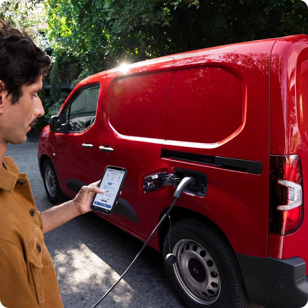 Side three‑quarter view of a Citroën ë‑Berlingo Van charging at a public station, showing practical electric use, connectivity and everyday convenience.