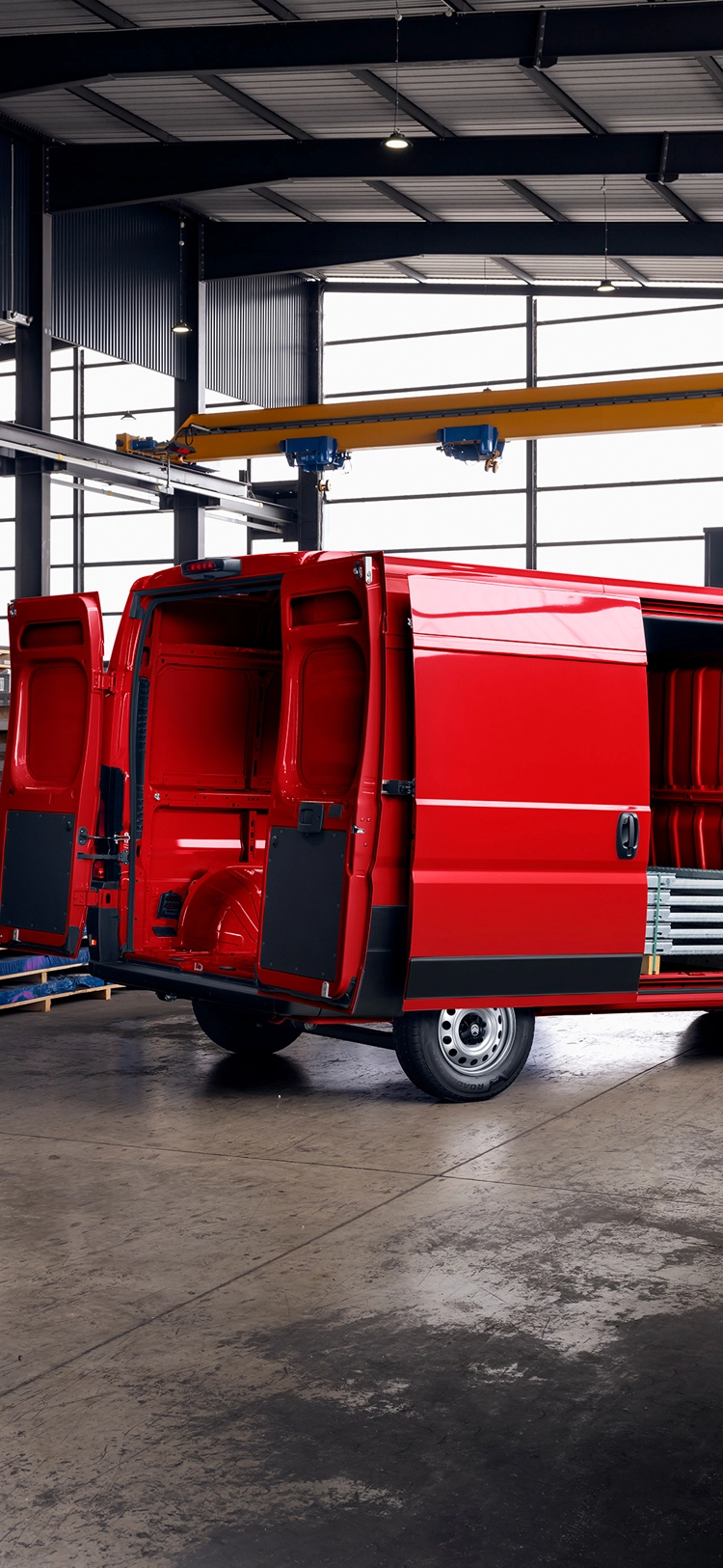 Dreiviertelansicht von hinten eines roten Citroën Jumper mit geöffneten Ladetüren in einem Lagerhaus, die den großen Laderaum, die Robustheit und die Vielseitigkeit für geschäftliche Zwecke hervorhebt.