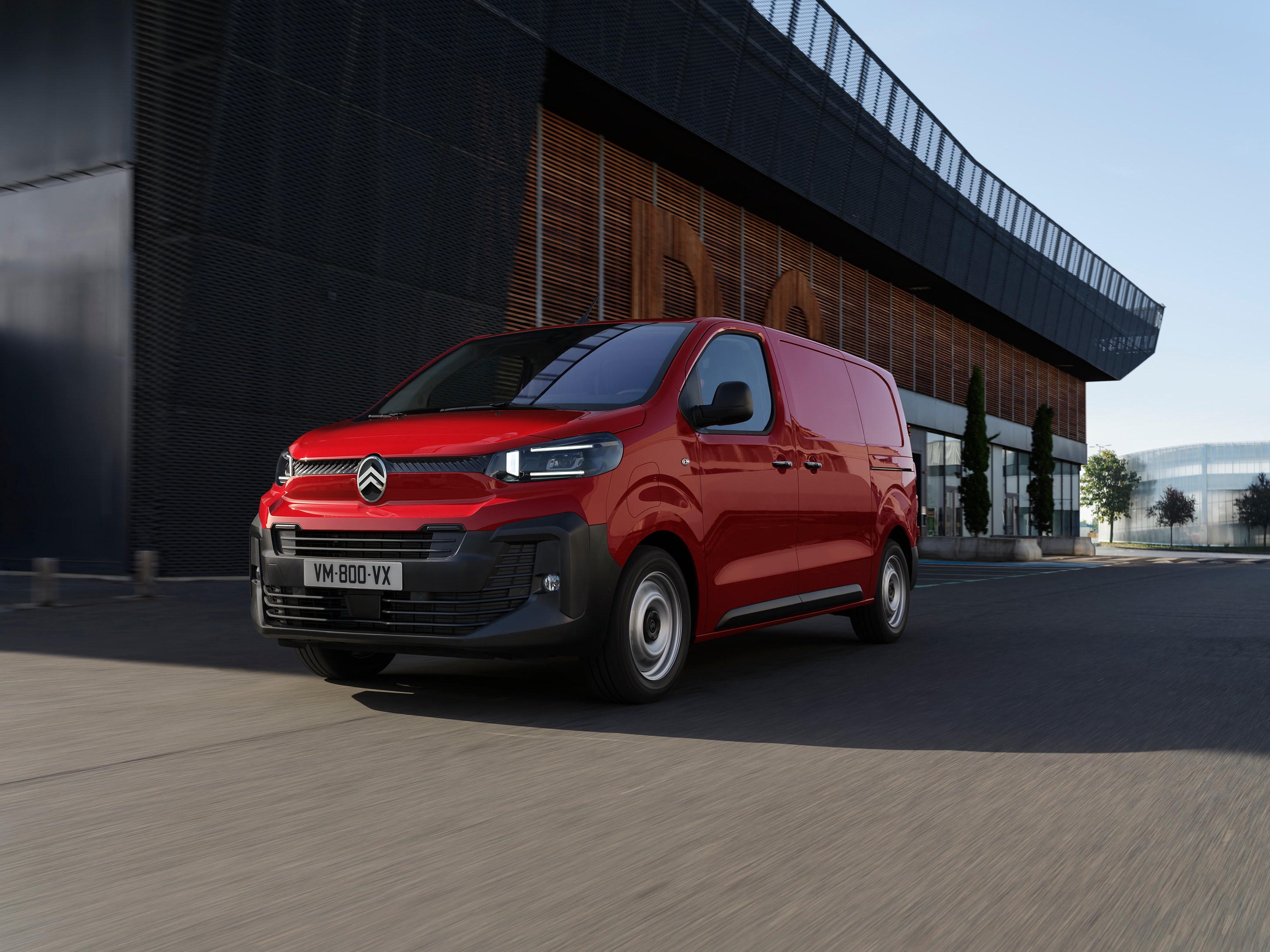 Dreiviertel-Frontansicht eines roten Citroën Jumpy vor einem modernen Gebäude geparkt, zeigt professionelles Design, Alltagstauglichkeit und selbstbewusstes Auftreten.