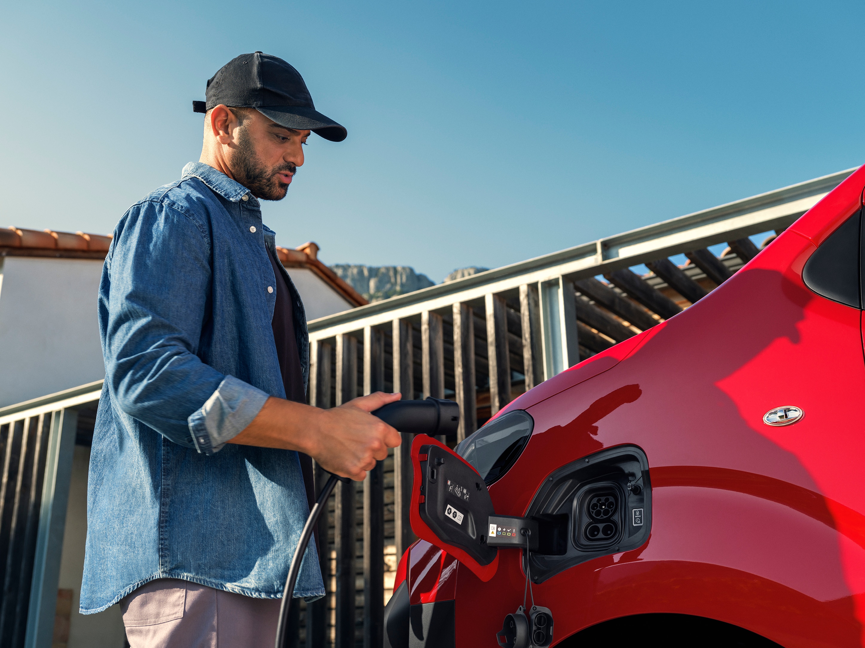 Seitenansicht eines roten Citroën ë-Jumpy beim Anschließen an eine Ladestation, zeigt einfaches elektrisches Laden, vernetzte Nutzung und praktische professionelle Mobilität.