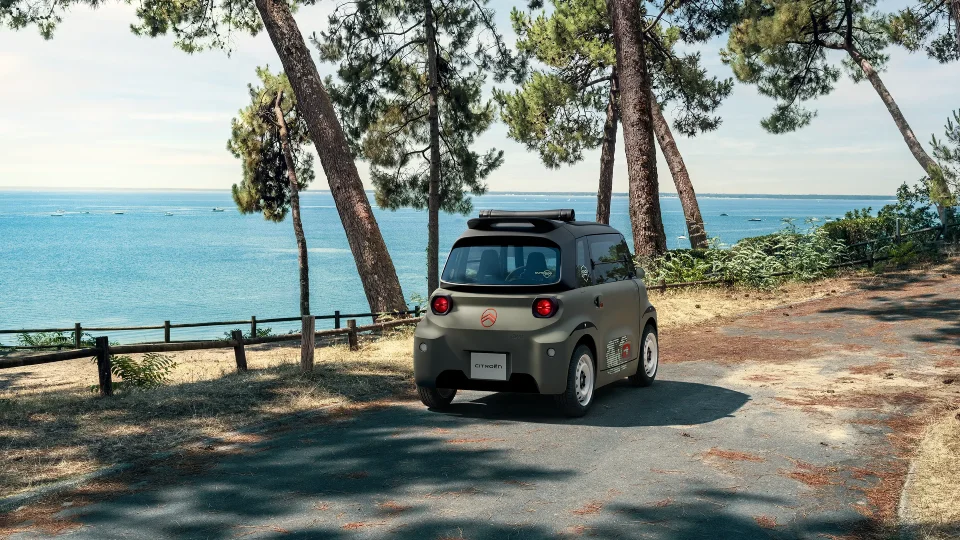 Dreiviertelansicht des Citroën Ami Outdoor von hinten an der Küste zeigt das elektrische Stadtfahrzeug mit geöffnetem Dach für Freizeitmobilität