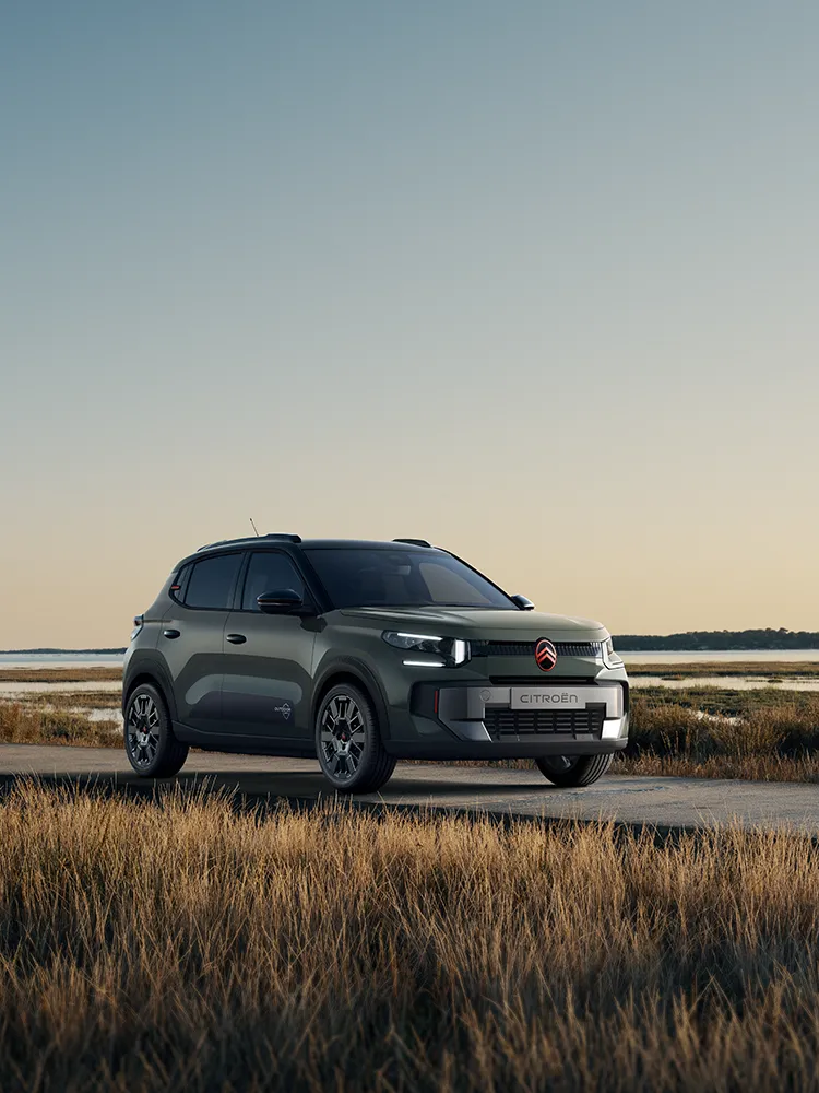 Front-Dreiviertelansicht des Citroën ë-C3 Outdoor mit LED-Lichtsignatur zeigt den Advanced Comfort SUV an einer Küsten-Feuchtlandschaft