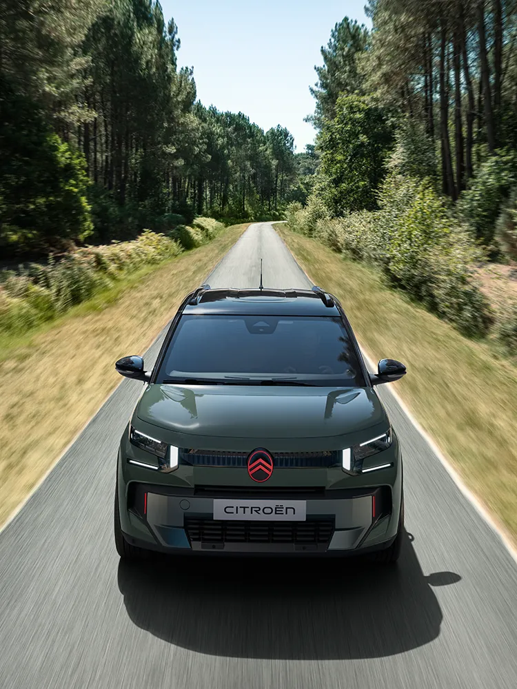 Frontansicht des Citroën ë-C3 Outdoor von oben mit LED-Lichtsignatur zeigt den kompakten SUV mit Advanced Comfort auf einer Waldstraße