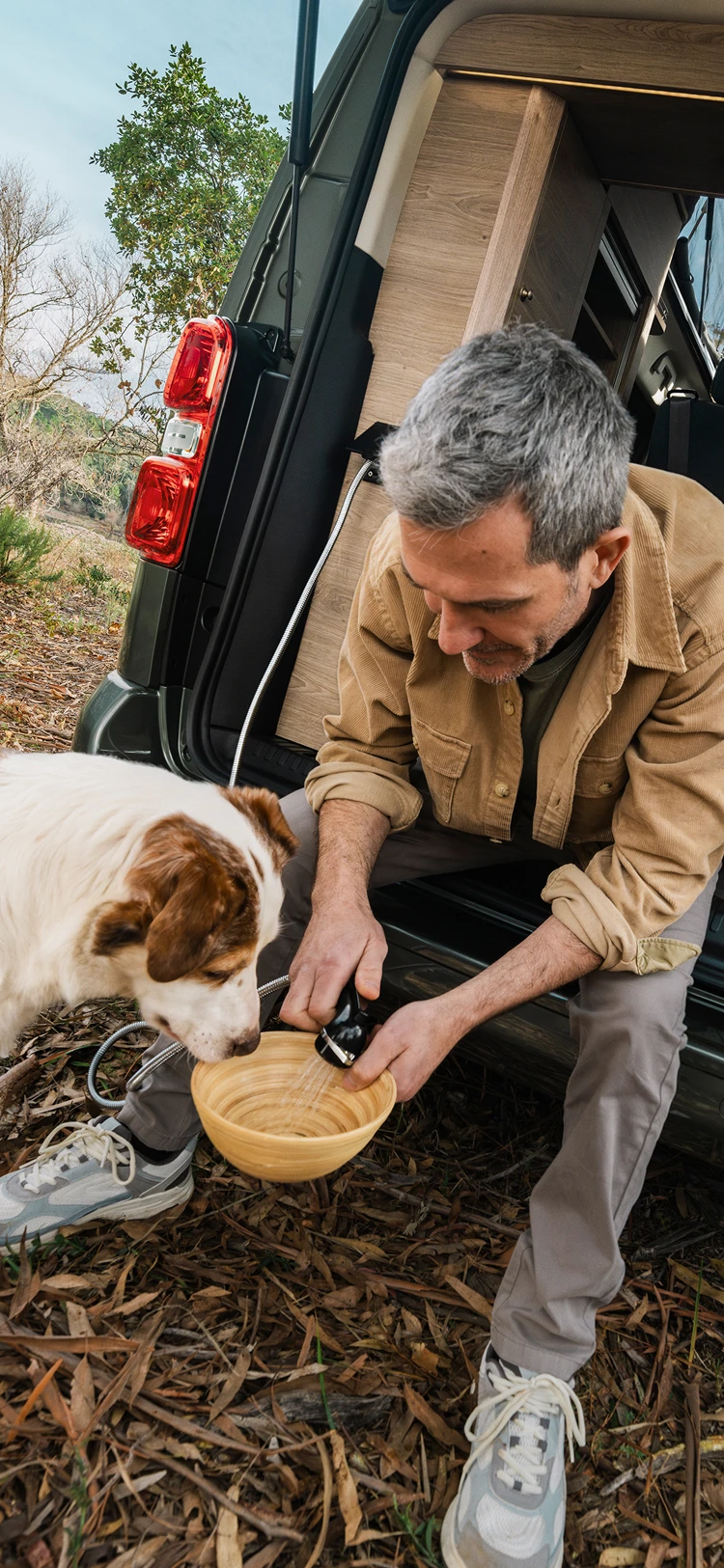Mann füttert einen Hund vom Heck eines Citroën Campervans in freier Natur