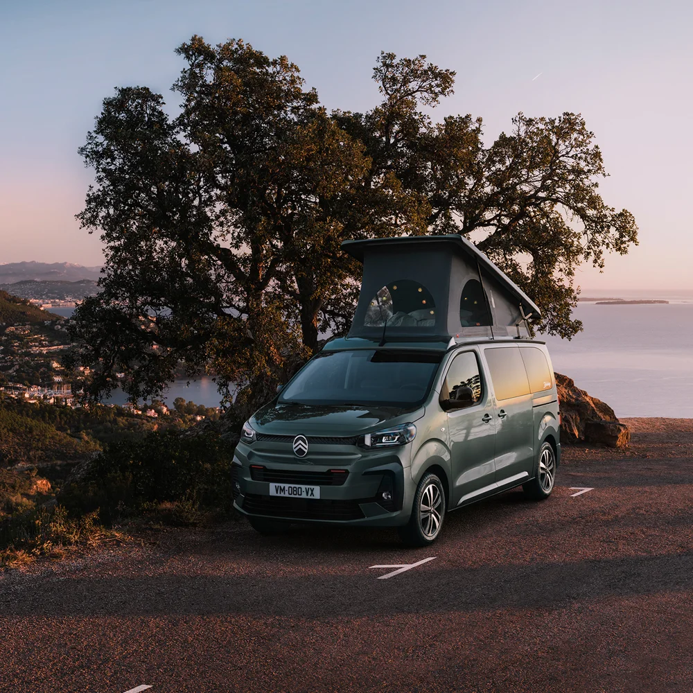 Citroën Campervan, geparkt auf einer malerischen Küstenstraße bei Sonnenuntergang, mit Bäumen und Hügeln im Hintergrund