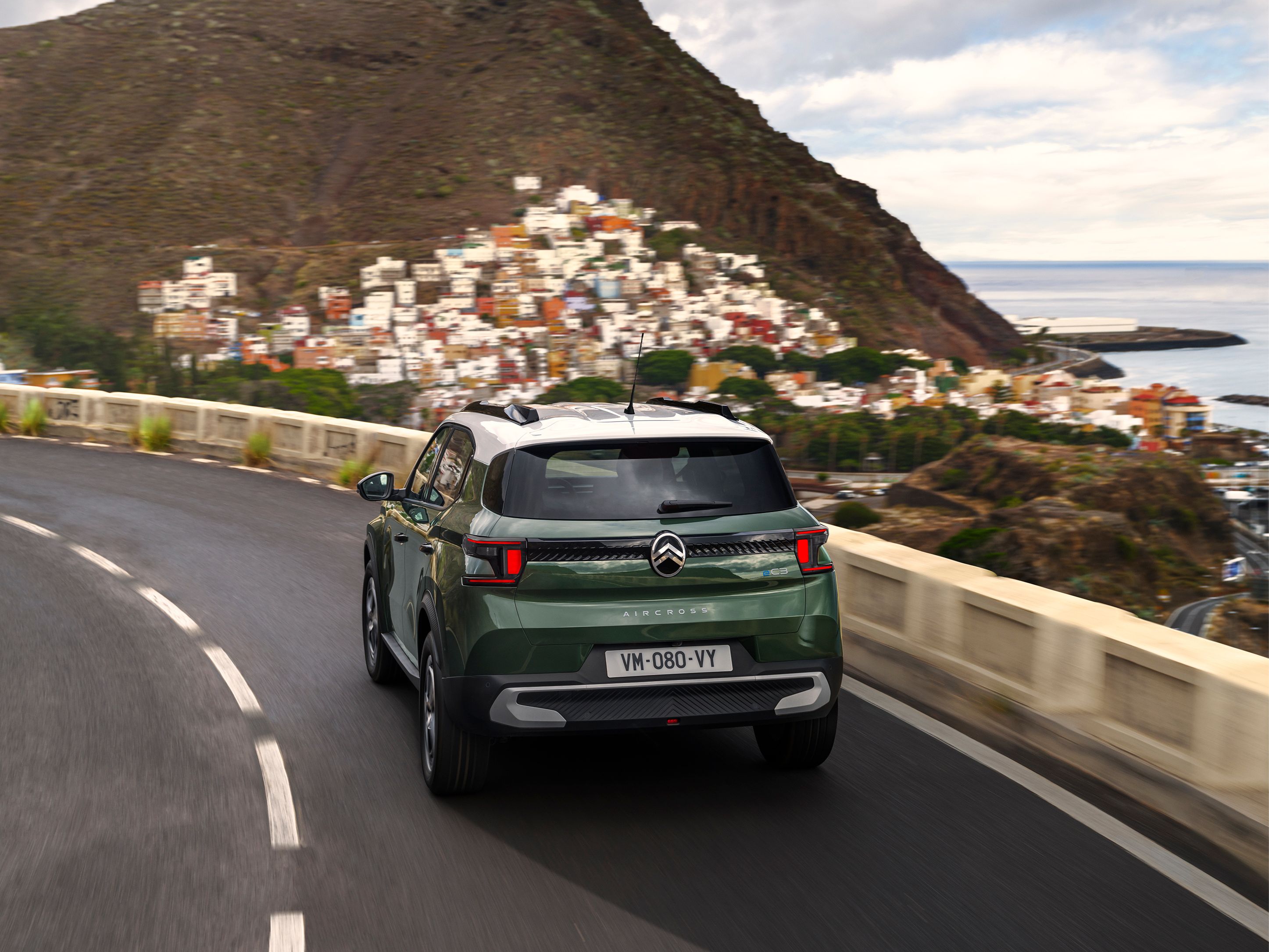 Dreiviertel-Heckansicht während der Fahrt des Citroën C3 Aircross SUV on a coastal road für sichere, smooth and erschwingliche Alltagsmobilität.