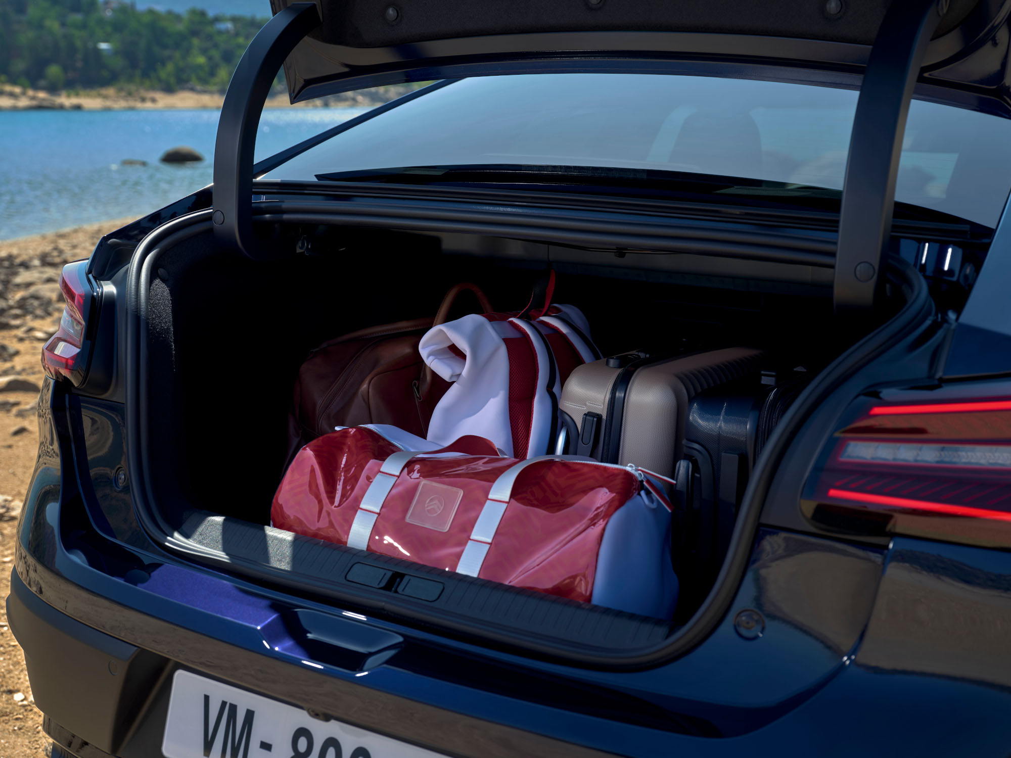 Geöffneter Kofferraum des Citroën C4 X beladen mit Reisetaschen neben einem Standort am See